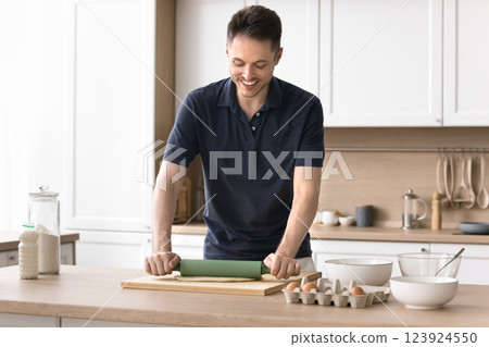 Smiling millennial male enjoy cooking at home kitchen roll dough Smiling millennial male enjoy cooking at home kitchen roll dough 123924550