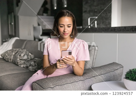 Pretty young woman using modern smartphone in living room Pretty young woman using modern smartphone in living room 123924557
