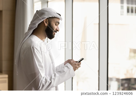 Arabian businessman in white dishdasha using modern smartphone Arabian businessman in white dishdasha using modern smartphone 123924606