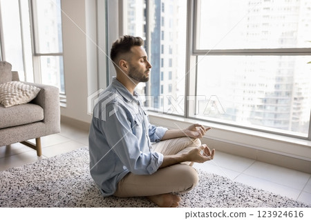 Young man meditating at home, relieving stress, boost inner balance Young man meditating at home, relieving stress, boost inner balance 123924616