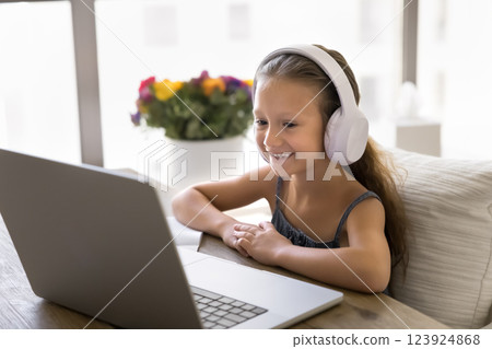 Little girl listens audio lesson through headphones, e-learning using laptop 123924868