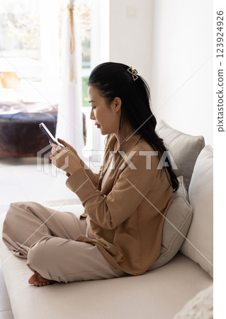 Serious young Vietnamese woman using mobile phone at home Serious young Vietnamese woman using mobile phone at home 123924926