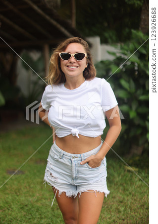A woman in sunglasses and a white crop top is in the grass A woman in sunglasses and a white crop top is in the grass 123926688