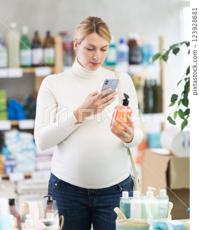 Pregnant customer scanning bottle of liquid soap with smartphone Pregnant customer scanning bottle of liquid soap with smartphone 123928681