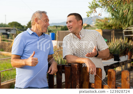 Two smiling men breezily chatting near wooden fence of rural house Two smiling men breezily chatting near wooden fence of rural house 123928724