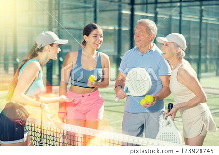 Three women and a man Padel tennis players speaking friendly in the court 123928745