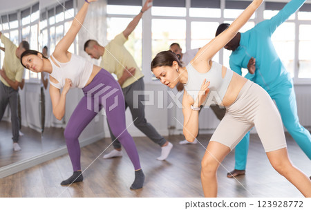 Pretty girl and multinational group of active young people practicing rock and roll dance in dance hall Pretty girl and multinational group of active young people practicing rock and roll dance in dance hall 123928772