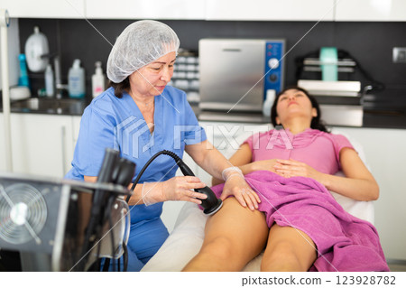 Highly qualified cosmetology doctor makes a young female patient of vacuum foot massage Highly qualified cosmetology doctor makes a young female patient of vacuum foot massage 123928782