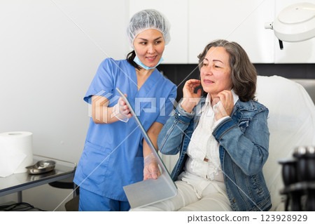 Satisfied elderly woman patient looks in the mirror after the procedure 123928929