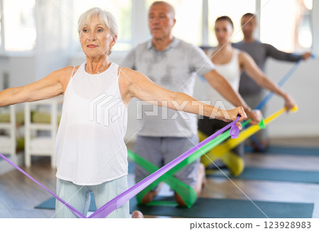 Elderly woman performs exercises with elastic band during Pilates strength training, kneeling 123928983