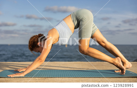 Yoga practice on embankment, female athlete fulfil carry out Adho Mukha Svanasana 123928991