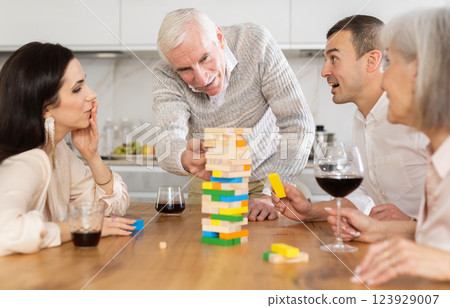 Group of mature spouses and son with girlfriend is playing board game with wooden blocks in kitchen 123929007