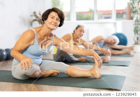 Old woman practicing seated side bend pose of yoga in training room during fitness classes 123929045