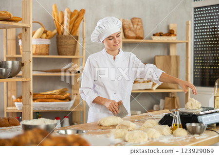 Teenage girl cutting and weighing dough on scales in bakehouse 123929069