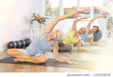 Old woman practicing lotus pose of yoga with side bend in training room 123929070