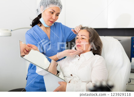 Female cosmetologist giving consultation to mature woman patient lying on couch in clinic Female cosmetologist giving consultation to mature woman patient lying on couch in clinic 123929118