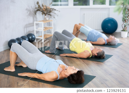 Elderly woman in company of hatha yoga lovers performs bridge pose, setu bandha sarvangasana 123929131
