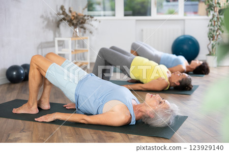 Old woman practicing bridge pose of yoga in training room during fitness classes Old woman practicing bridge pose of yoga in training room during fitness classes 123929140
