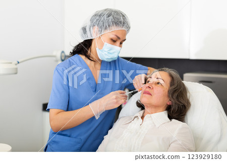 Cosmetologist injecting facial filler into skin to elderly female client 123929180