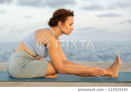 Yoga practice on embankment, female athlete fulfil carry out Pashchimottanasana 123929185