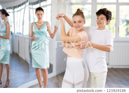 Experienced dance teacher teaching ballroom dancing to a couple of teenagers in studio Experienced dance teacher teaching ballroom dancing to a couple of teenagers in studio 123929186
