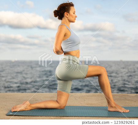Yoga practice on embankment, female athlete fulfil carry out Anjaneyasana Yoga practice on embankment, female athlete fulfil carry out Anjaneyasana 123929261