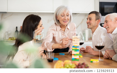 Group of mature spouses and son with girlfriend is playing board game with wooden blocks in kitchen 123929313