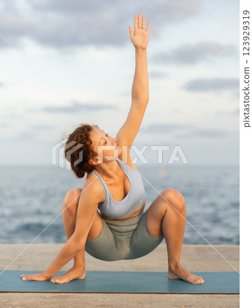Yoga practice on embankment, female athlete fulfil carry out Malasana 123929319