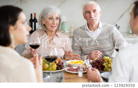 Mature married couple are sitting at table, enjoying food and wine with middle-aged guests. Mature married couple are sitting at table, enjoying food and wine with middle-aged guests. 123929350