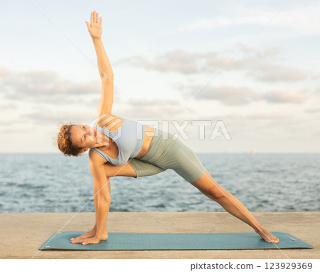 Yoga practice on embankment, female athlete fulfil carry out Parivritta Parshvakonasana 123929369