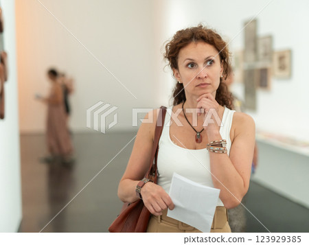 Middle-aged woman looking at pictures on wall in museum Middle-aged woman looking at pictures on wall in museum 123929385