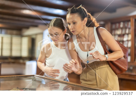 Young woman with teen daughter visitors stands near horizontal glass display case Young woman with teen daughter visitors stands near horizontal glass display case 123929537