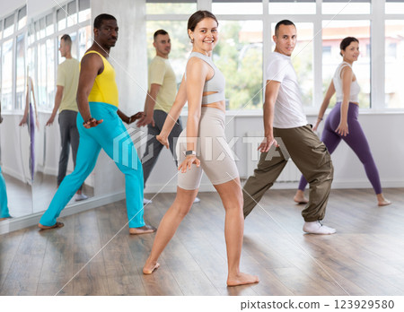 Smiling woman with multinational group active people enthusiastically training social latin cha-cha-cha dance movements in dance salon Smiling woman with multinational group active people enthusiastically training social latin cha-cha-cha dance movements in dance salon 123929580