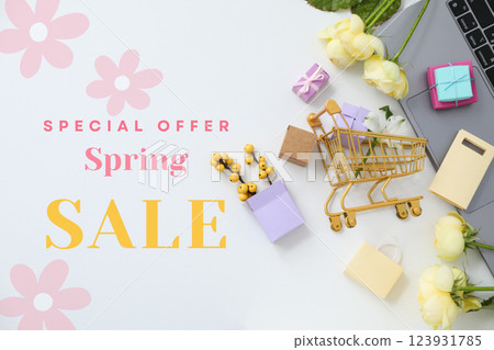 Hello spring, laptop, shopping cart figurine, gift boxes and flowers on a light background, top view, with text 123931785