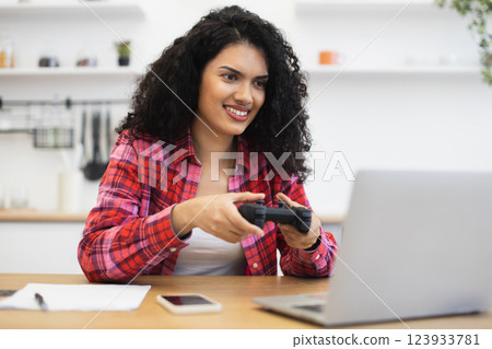 Young African American woman playing video game on laptop computer using game controller in modern home setting 123933781
