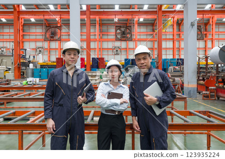 Three factory worker stand confidently in a vibrant industrial setting, discussing plan and strategy for enhancing operational efficiency during the day. 123935224