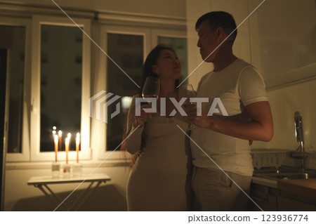 Romantic couple sharing wine and intimate moments in candlelit kitchen 123936774