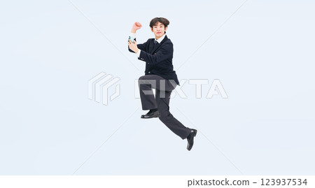 Full-body photo of a male student in uniform jumping with a smartphone Full-body photo of a male student in uniform jumping with a smartphone 123937534