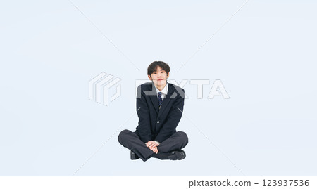 Full-body photo of a male student in uniform sitting 123937536