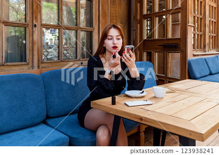 A girl in a cafe at a table paints her lips with red lipstick A girl in a cafe at a table paints her lips with red lipstick 123938241