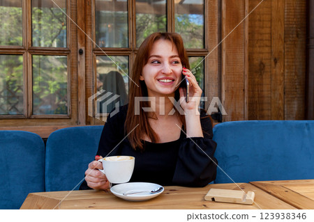 A girl in a cafe at a table talking on the phone A girl in a cafe at a table talking on the phone 123938346