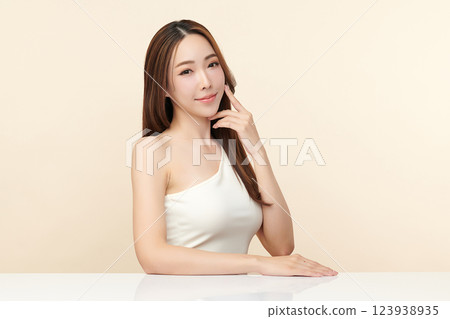 A beautiful young Asian woman with clean, fresh skin against a beige background. She represents beauty, skincare, and spa treatments. 123938935