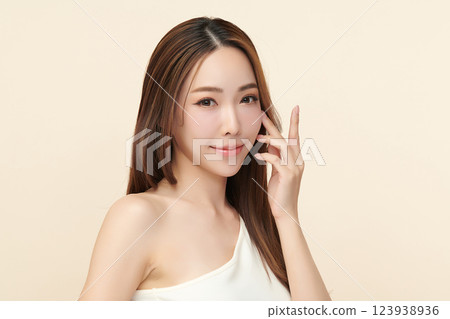 A beautiful young Asian woman with clean, fresh skin against a beige background. She represents beauty, skincare, and spa treatments. 123938936