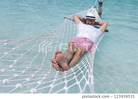 A young man in summer clothes and a hat is lying in a hammock in clear sea water 123939535