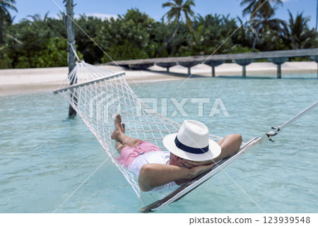 A young man in summer clothes and a hat is lying in a hammock in clear sea water 123939548