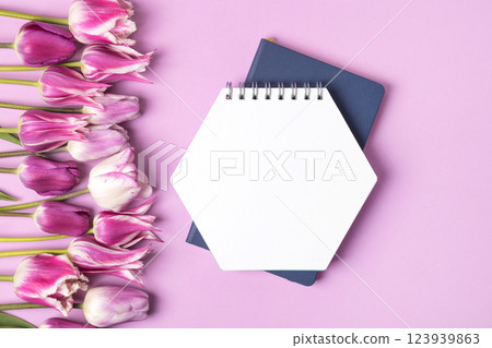 Open paper notebook with empty page with purple and white tulips on purple background. Top view, flat lay, work space on purple background. 123939863