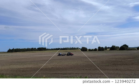 Beautiful view from the window of a moving car on the field where the tractor stands on a recently harvested wheat field. Blue sky with clouds. 123940272