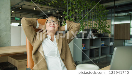 A senior businesswoman feeling stressed, sitting in an office chair and massaging her temples, experiencing work-related fatigue in a modern corporate workspace 123941740