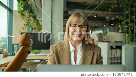 A senior businesswoman feeling stressed, sitting in an office chair and massaging her temples, experiencing work-related fatigue in a modern corporate workspace 123941741