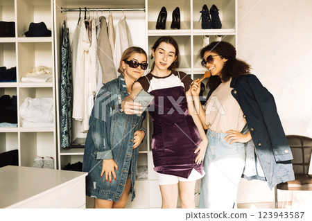 Charismatic teenage girls of different races collect clothes for the wardrobe. Multiethnic girls take selfies in the dressing room at home. Charismatic teenage girls of different races collect clothes for the wardrobe. Multiethnic girls take selfies in the dressing room at home. 123943587